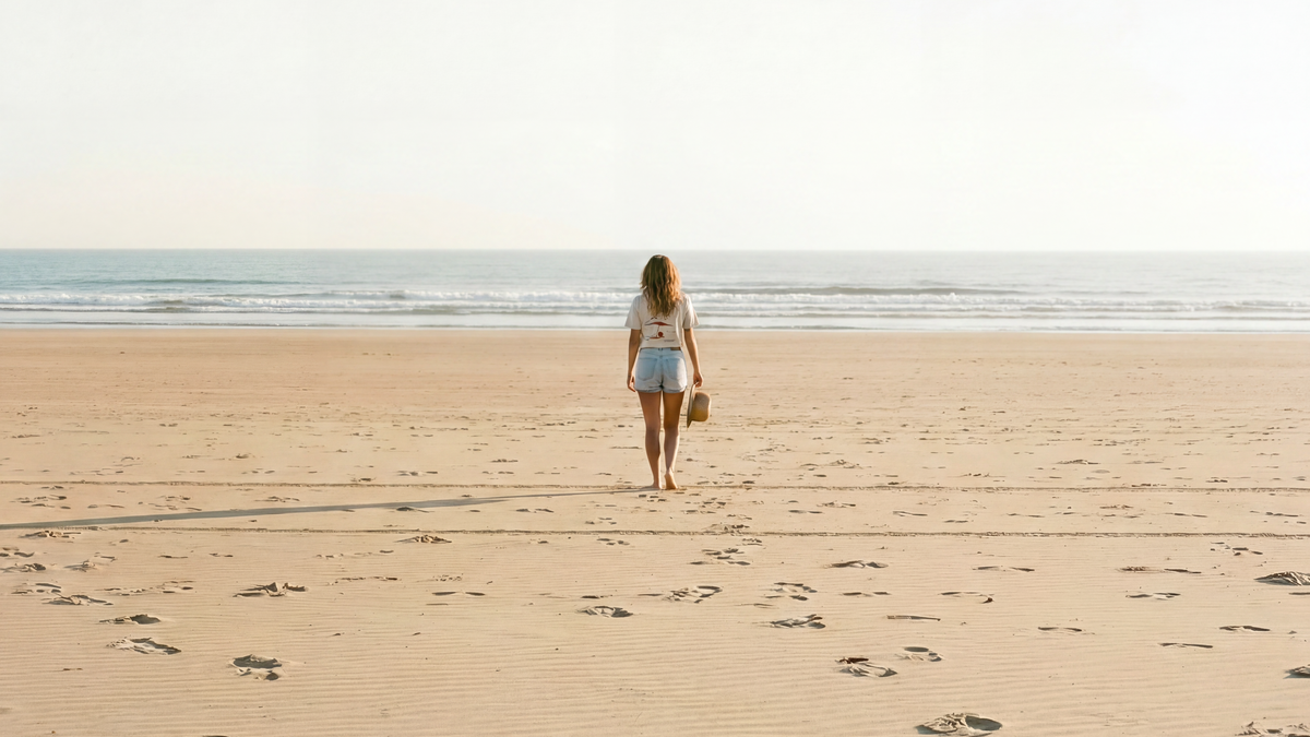 Person walking alone on a sandy beach with clear sky